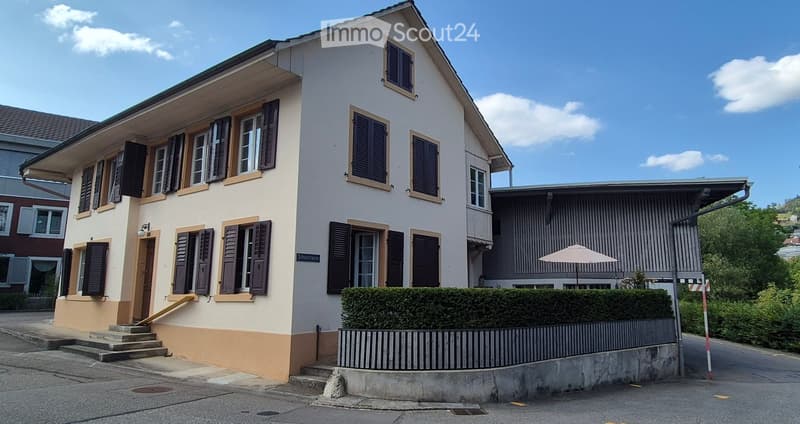 Two-story house with white walls, dark shutters, and a raised ground floor accessed by steps.