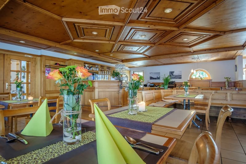 Cozy restaurant interior with wooden tables, chairs, floral centerpieces, and neatly arranged table settings.