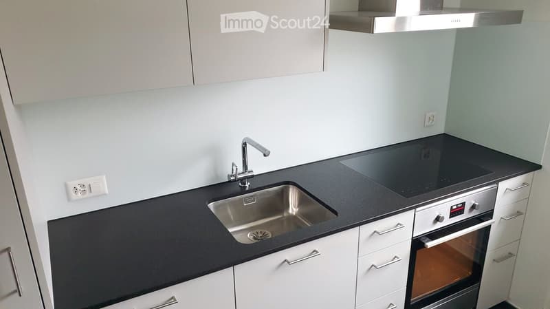 Modern kitchen with black countertops, white cabinets, stainless steel sink, faucet, and built-in oven.