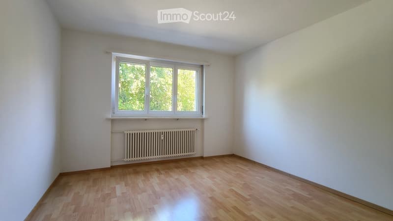 Empty room with wooden flooring, white walls, and a window with a radiator below it.