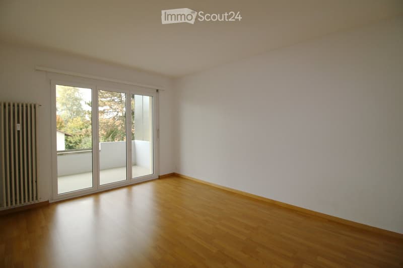 Empty room with wooden flooring, white walls, and large sliding glass doors leading to a balcony.