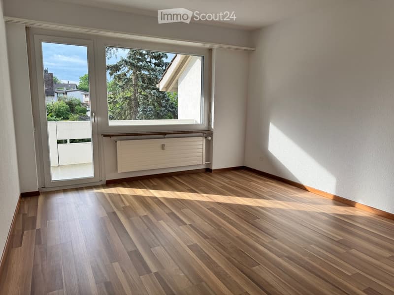 Empty room with wooden flooring, large windows, and a radiator. No furniture or equipment present.
