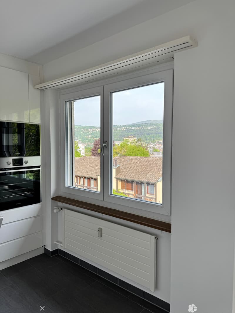 Empty room with dark tiled floor, white walls, large windows with wooden sill, radiator, and built-in oven.