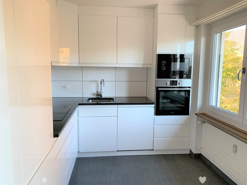 Modern kitchen with white cabinets, stainless steel appliances, and a black countertop.