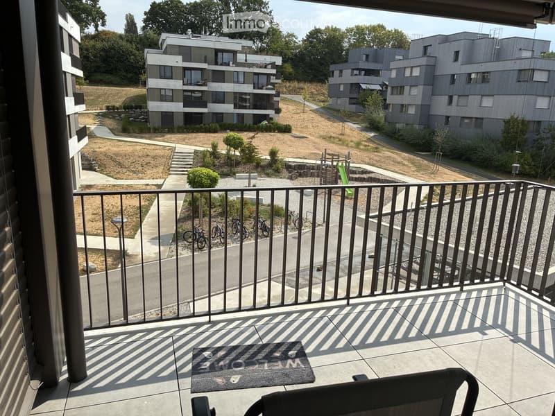 Balcony with a view of a modern residential complex, featuring a chair and a doormat.