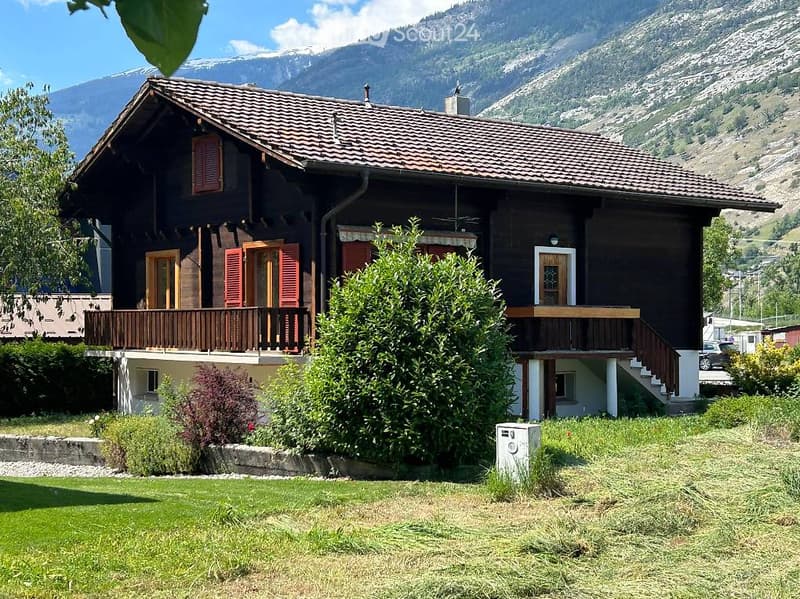 Traditional wooden house with a tiled roof, multiple windows, and a balcony overlooking a scenic mountain view.