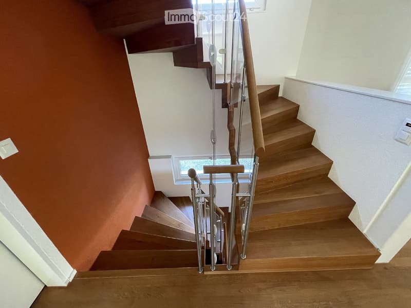 Wooden staircase with metal railing, leading to an upper level, with a window providing natural light.