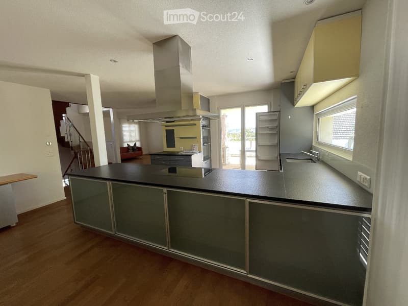 Modern kitchen with grey cabinets, black island, stainless steel appliances, and a view to a balcony.