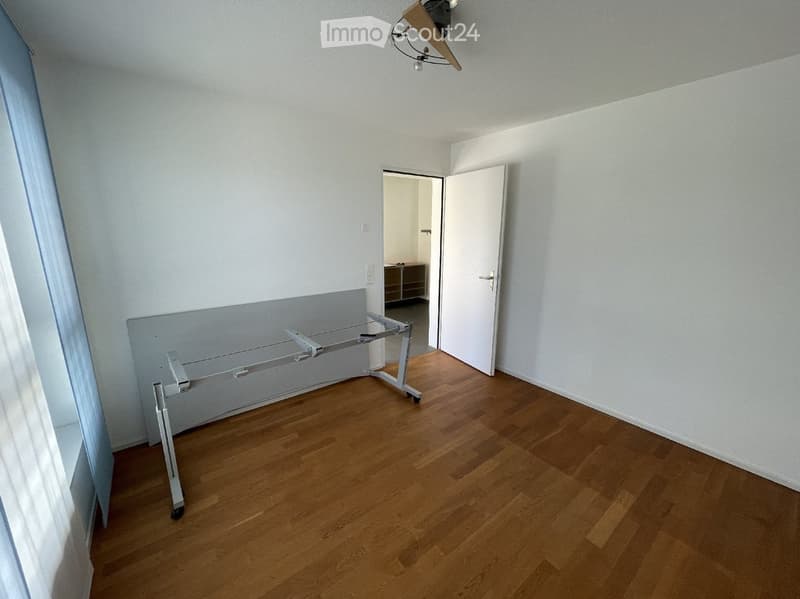 Empty room with wooden flooring, white walls, and a partially visible adjacent room with a small cabinet. No furniture or personal items are present.