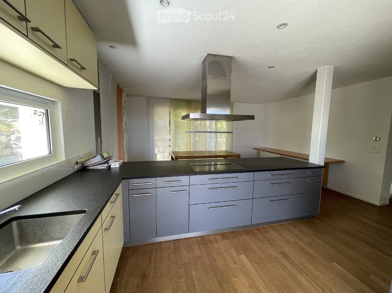 Modern kitchen with grey cabinets, black countertop, stainless steel stove, and wooden floor.