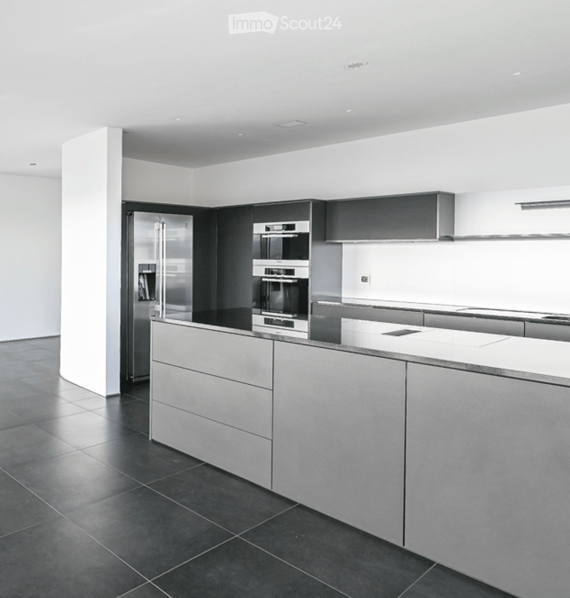 Modern kitchen with sleek, minimalist design featuring a large island, stainless steel appliances, and dark tiled flooring.
