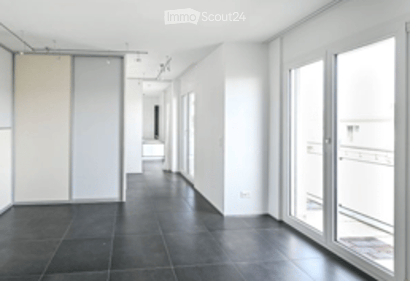 Empty corridor with white walls, dark tiled floor, large windows, and doors leading to other rooms.