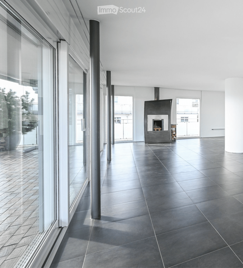Open, modern space with large glass windows, dark tiled floor, and a central fireplace.