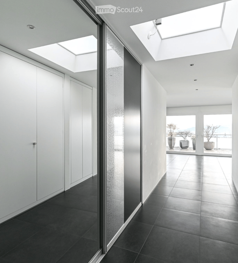 Modern hallway with black tiled flooring, white walls, large glass doors leading to a balcony, and built-in white cabinetry.