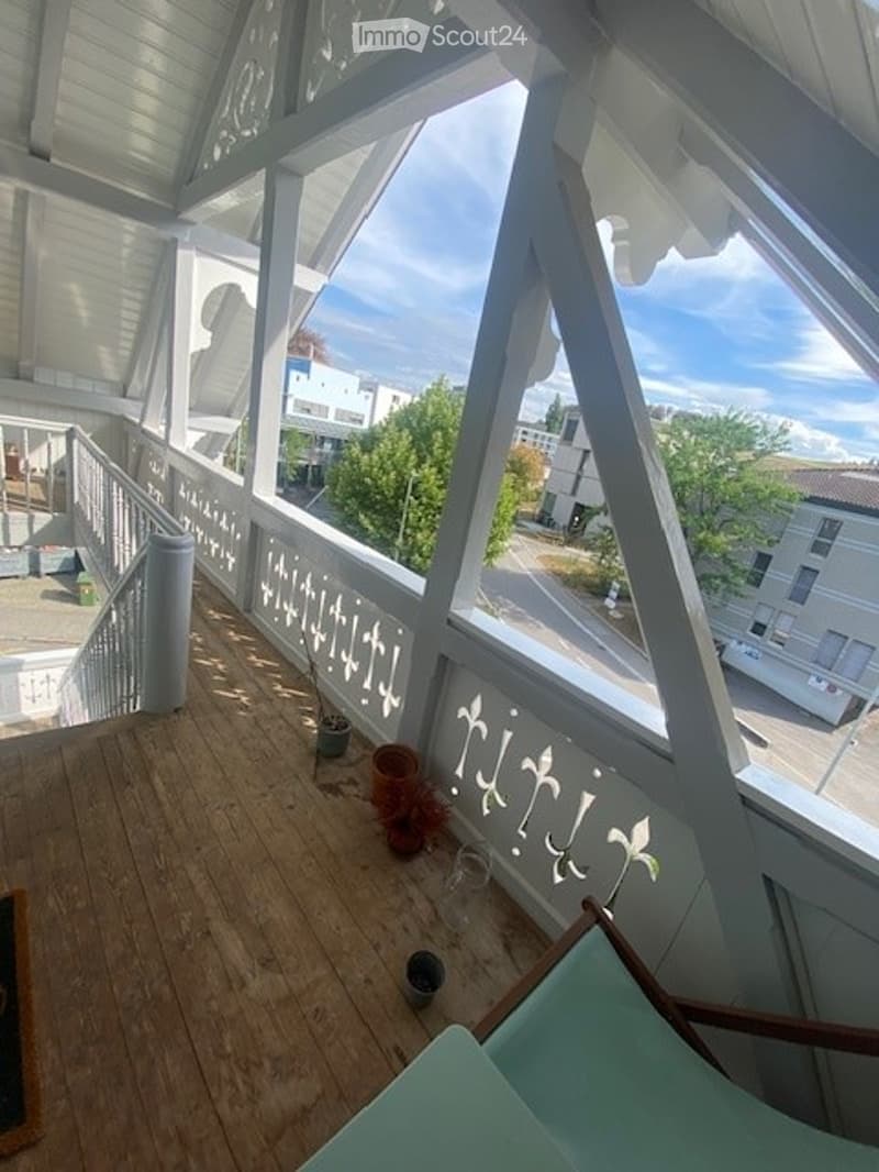 Balcony with wooden floor, white railings, and a view of the street and surrounding buildings.