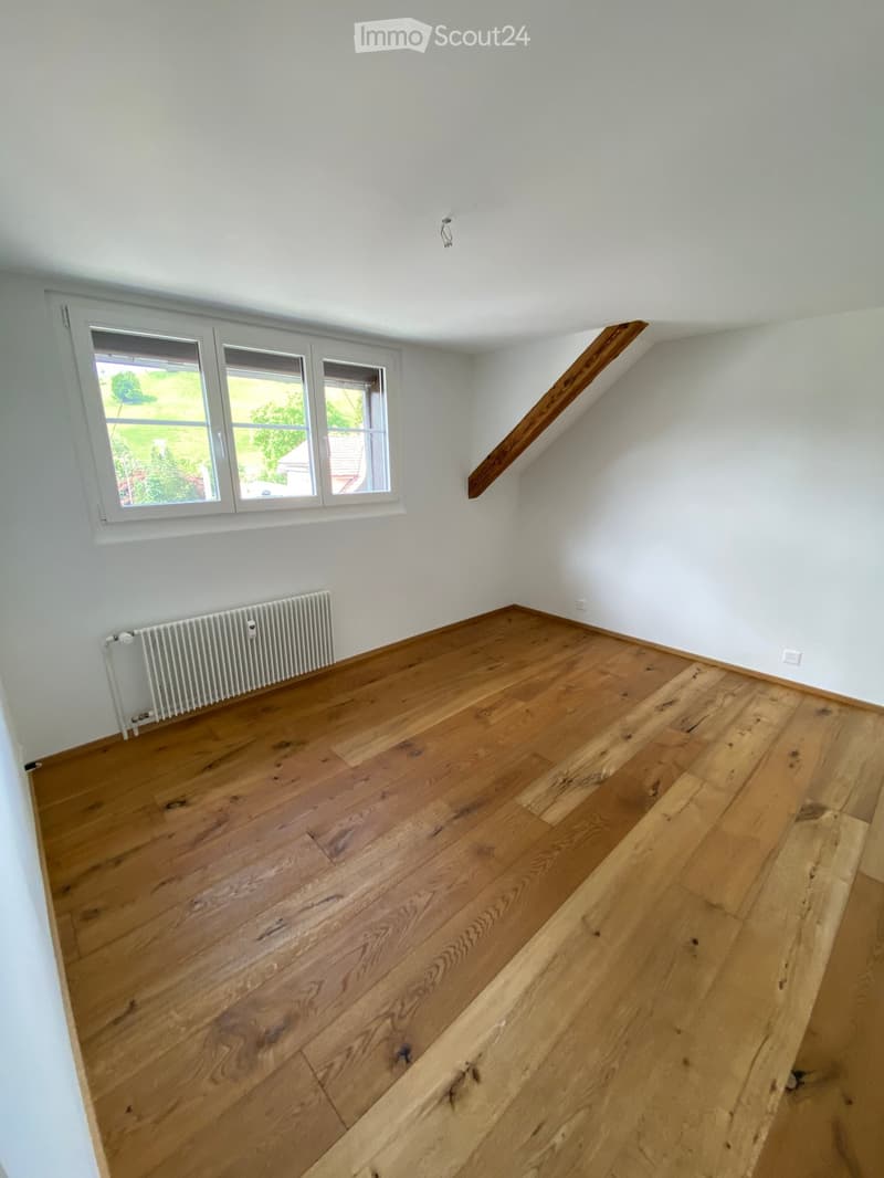 Empty room with wooden flooring, white walls, and a window with a view of greenery. No furniture or equipment present.