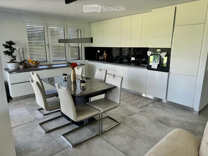 Modern kitchen and dining area with white cabinets, a black countertop, a glass dining table with six chairs, and decorative items on the counter.