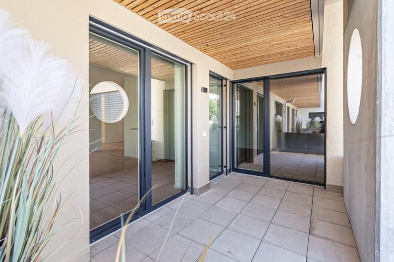 Modern balcony with large glass sliding doors, wooden ceiling, tiled floor, and circular mirrors on walls.