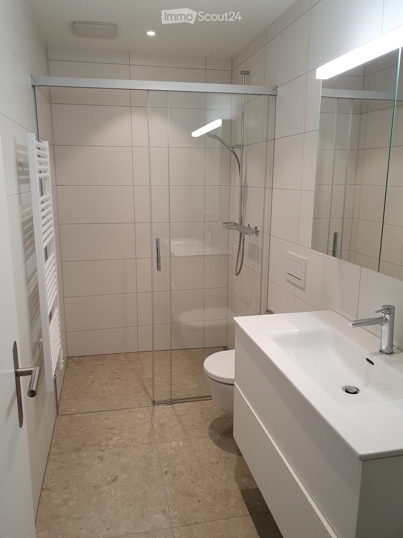 modern bathroom with white tiles, glass shower enclosure, white sink, white toilet, white towel rack