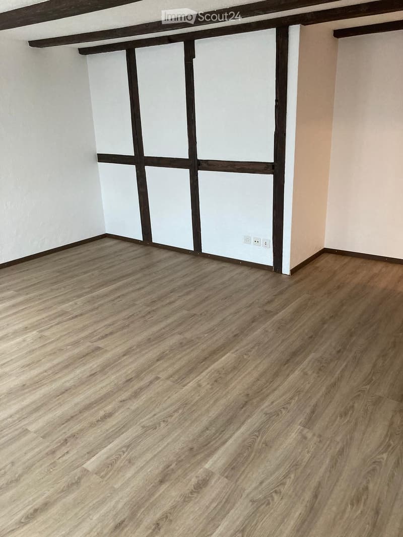 Empty room with light wooden flooring, white walls, and a wooden door frame.