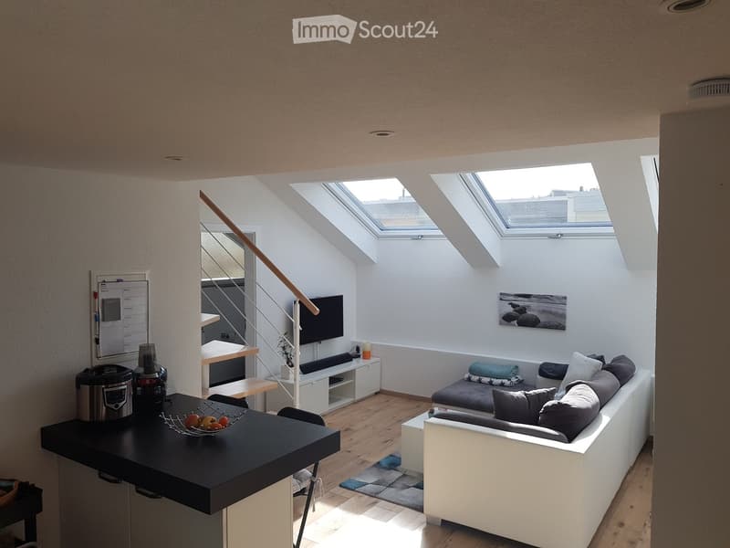 Modern living room with white walls, wooden floor, large skylights, sofa, coffee table, TV, and small kitchen area.
