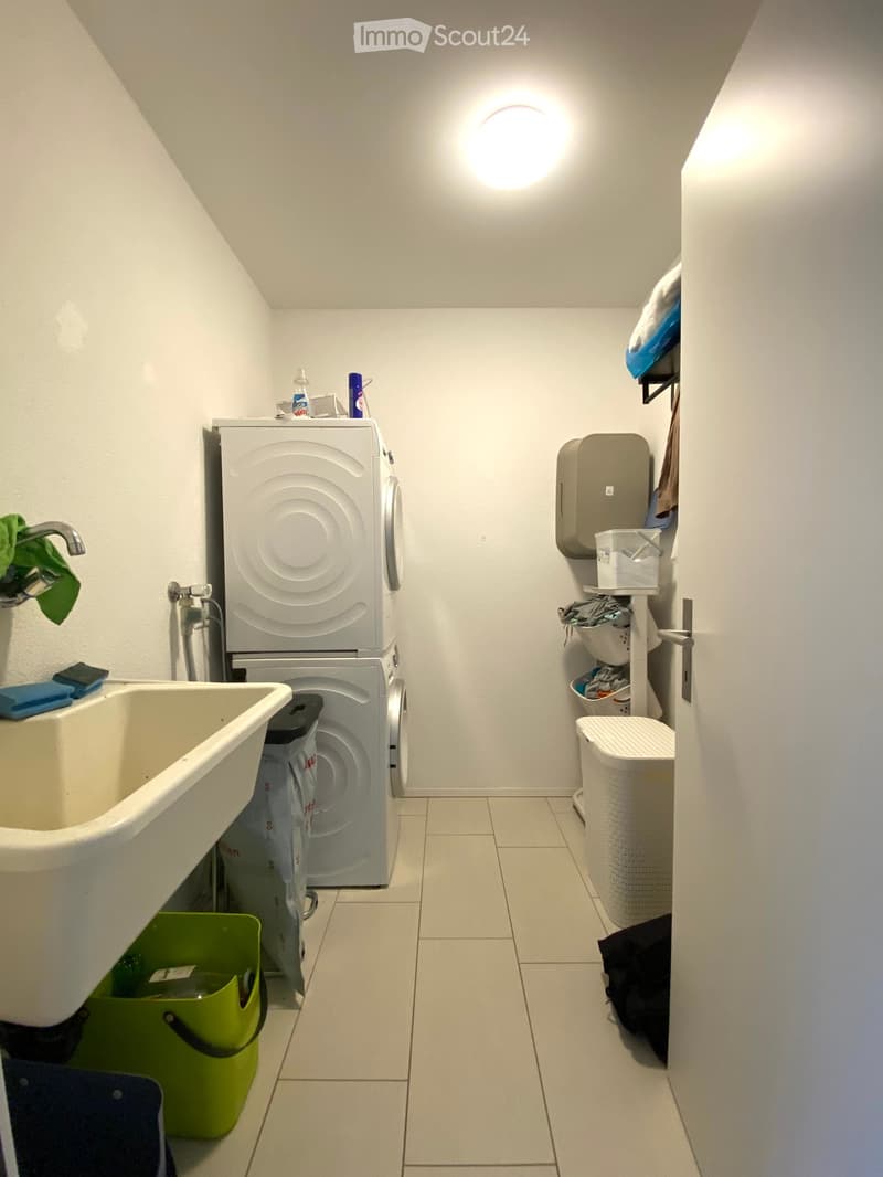 Bathroom with a bathtub, stacked washing machine and dryer, shelves, and laundry basket.