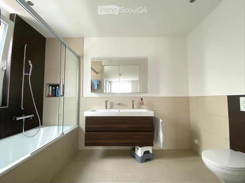 Modern bathroom with a bathtub, double sink, toilet, mirror, and a glass-enclosed shower area.
