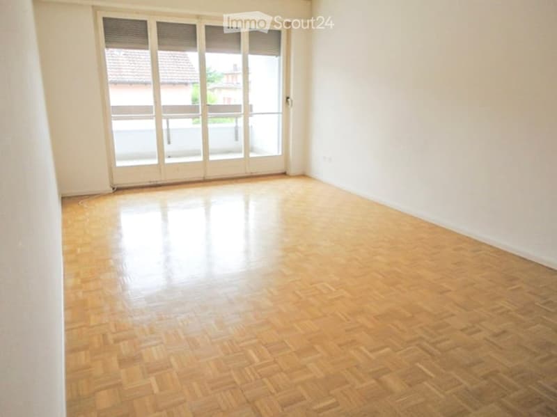 Empty room with wooden parquet flooring, white walls, and large glass sliding doors leading to a balcony.