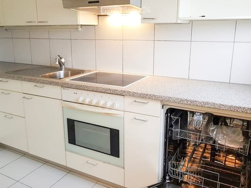 Modern kitchen with white cabinets, granite countertops, stainless steel sink, built-in oven, and open dishwasher.