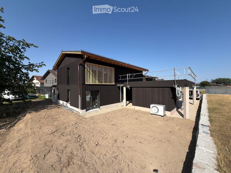 Modern two-story house with dark wooden exterior, large balcony on the upper floor, and a raised ground floor.