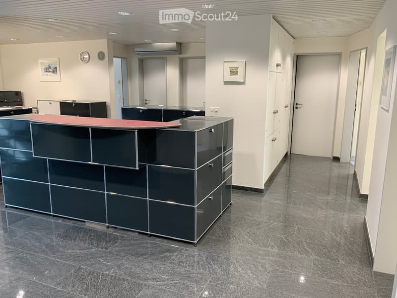 Modern reception area with a sleek black reception desk, white walls, grey tiled floor, and several closed doors leading to other rooms.