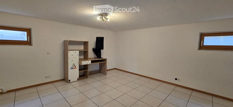 Small room with tiled floor, two windows, a refrigerator, a wooden shelf, a desk, and a chair.