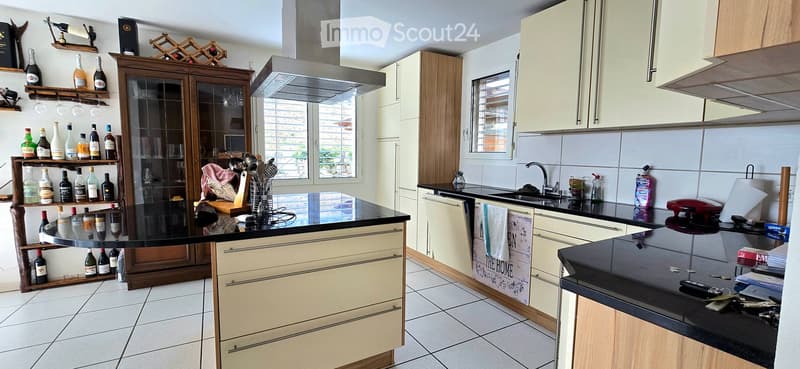 Modern kitchen with light-colored cabinets, black countertops, and a central island. Features include a wine rack, a sink with a faucet, and various kitchen appliances.