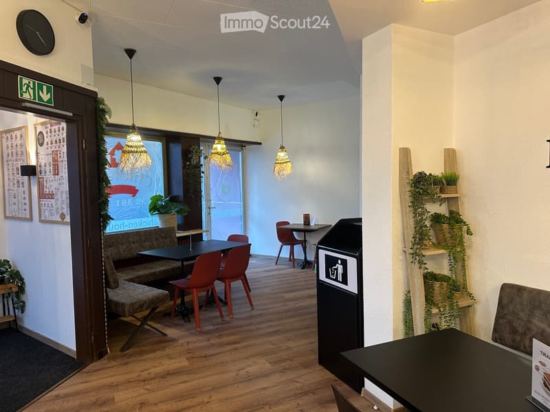 Modern restaurant interior with wooden flooring, pendant lights, tables, chairs, and a bench seating area.