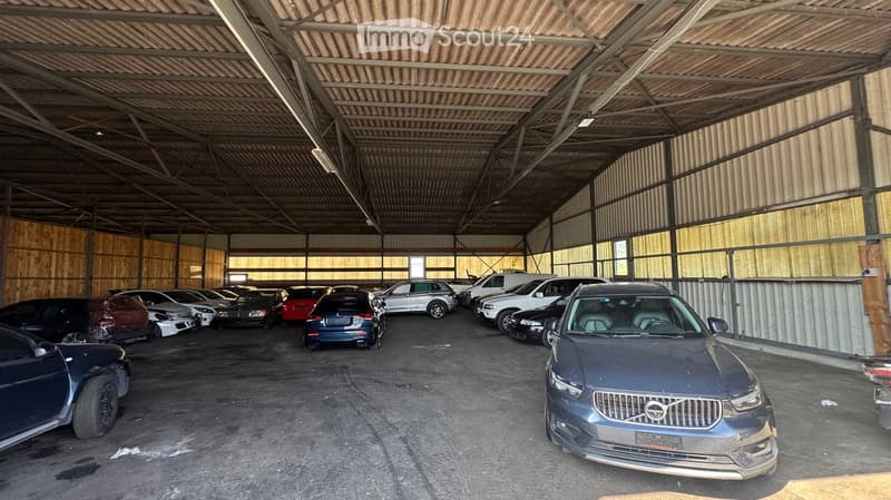 Large indoor garage with multiple parked cars, wooden walls, and a high ceiling with exposed beams.