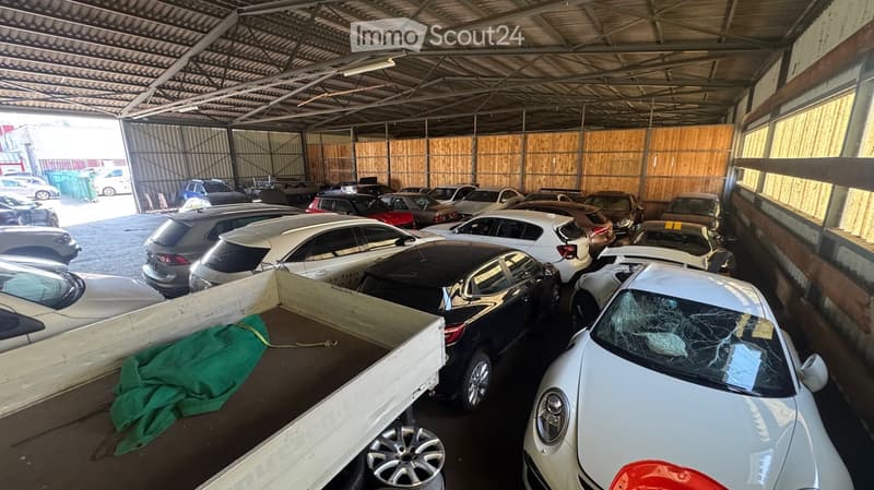 Indoor parking area with multiple cars, metal roof, wooden walls, and a green tarp on the floor.