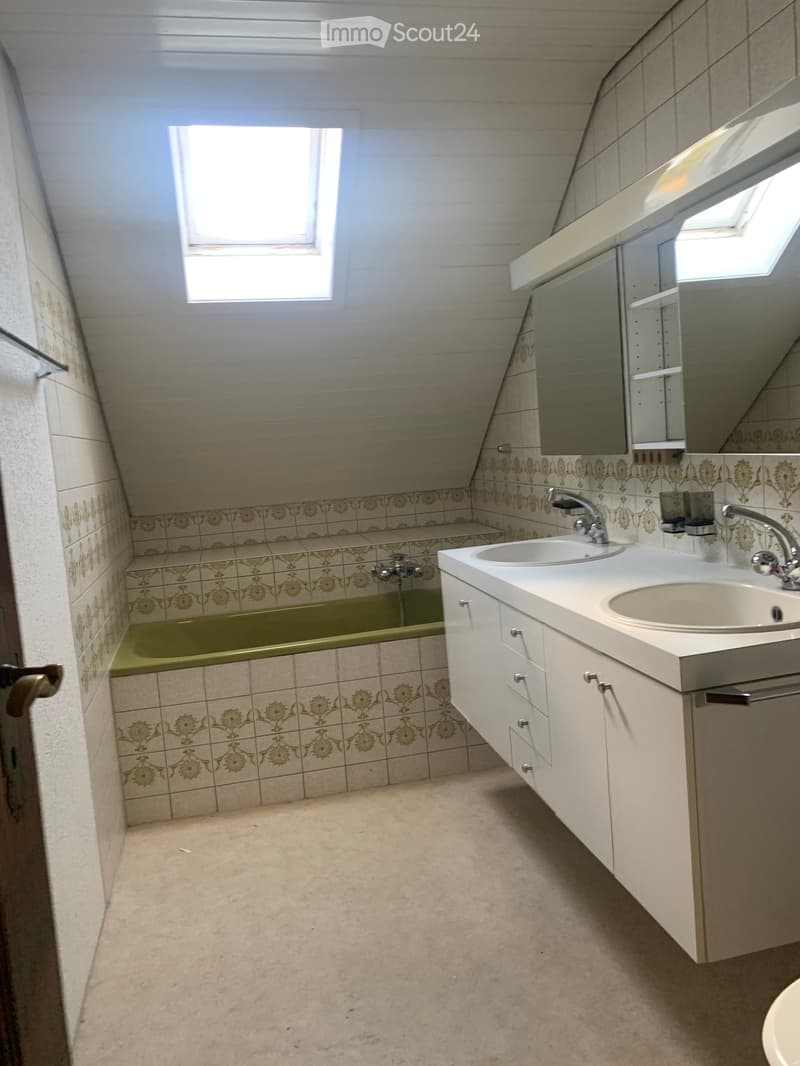 Bathroom with a green bathtub, white sink, and mirrored cabinet. The walls are tiled with a floral pattern, and the floor is light-colored.