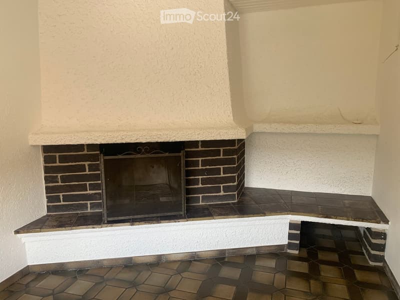 Empty room with a fireplace, white textured walls, and tiled flooring.