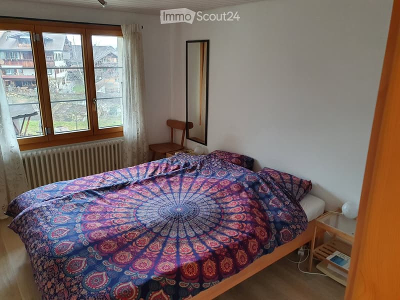 Cozy bedroom with a wooden bed, colorful bedspread, wooden chair, mirror, nightstand, and radiator.