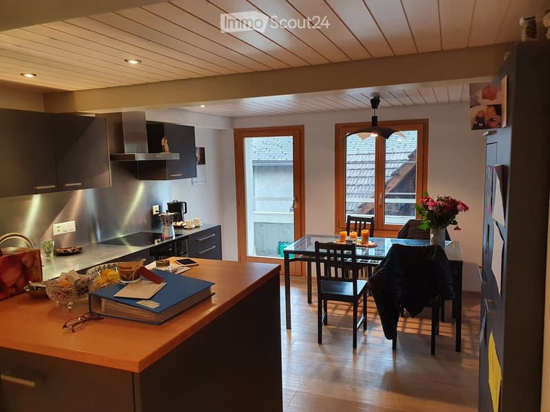 Modern kitchen and dining area with wooden floors, stainless steel appliances, a central island, and a dining table with chairs.