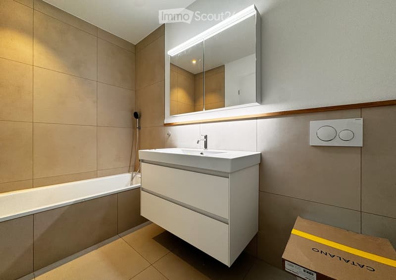 Modern bathroom with a white sink, mirror with LED lighting, bathtub, and a control panel for the shower.