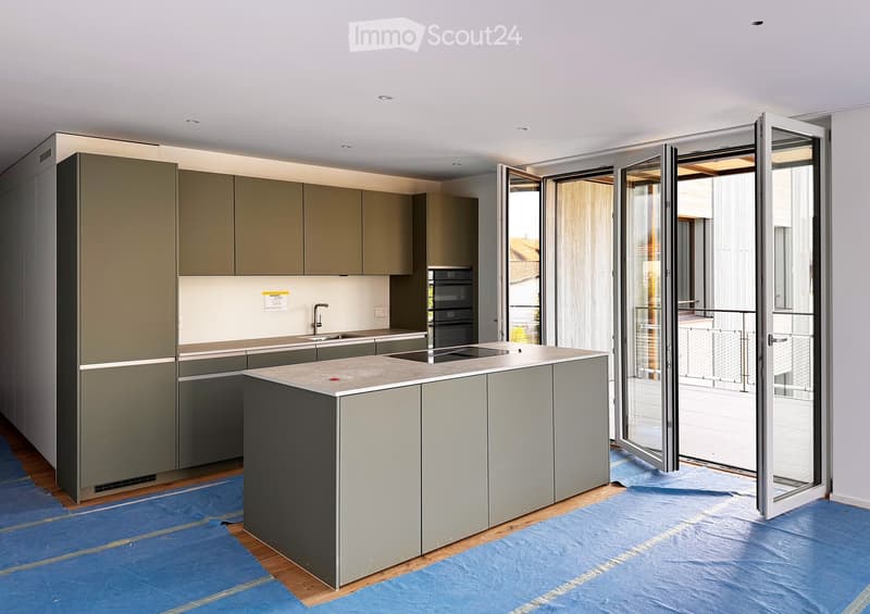 Modern kitchen with grey cabinets, central island, sink, and open sliding doors leading to a balcony.
