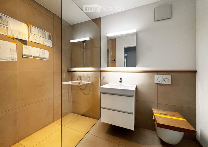 Modern bathroom with two sinks, a large mirror, a glass-enclosed shower, and a toilet partially covered by a cardboard box.