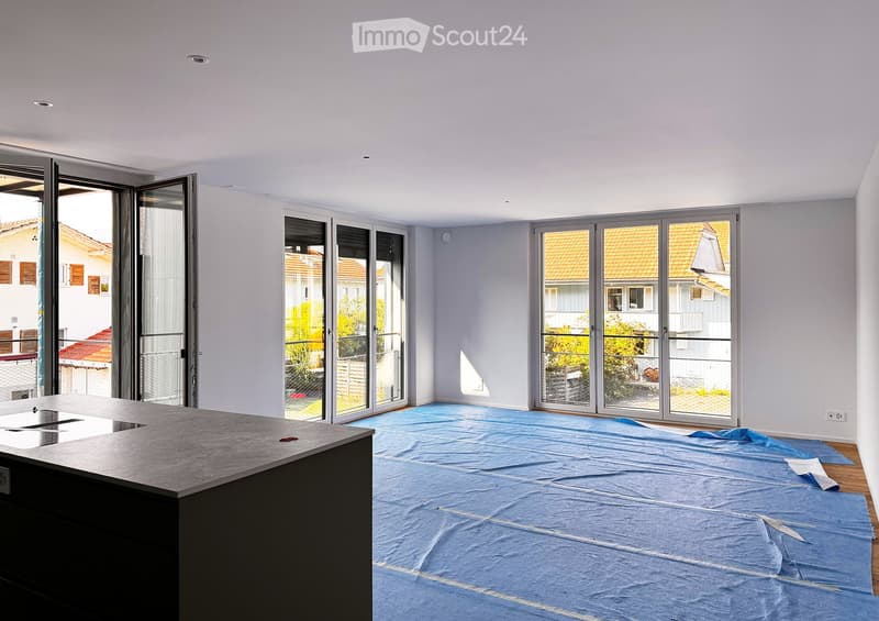 Empty room with a kitchen island, large windows, and a blue protective sheet covering the floor.