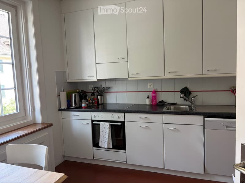 Modern kitchen with white cabinets, stainless steel appliances, and a black countertop. Includes an oven, dishwasher, sink, and various kitchen items.