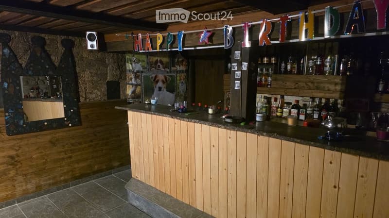 A cozy bar area with wooden counter, shelves filled with bottles, a mirror, and a "Happy Birthday" banner.