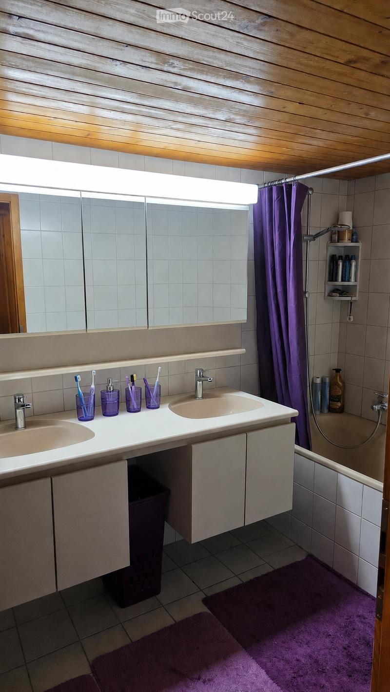 Bathroom with double sink, mirror, toothbrush holders, soap dispenser, bathtub with shower curtain, and purple rugs.