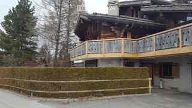 A large, multi-story wooden building with a prominent balcony and a well-maintained hedge in the foreground.