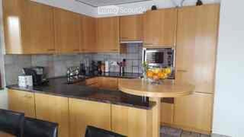 Modern kitchen with light wooden cabinets, black countertops, and a small seating area with chairs.