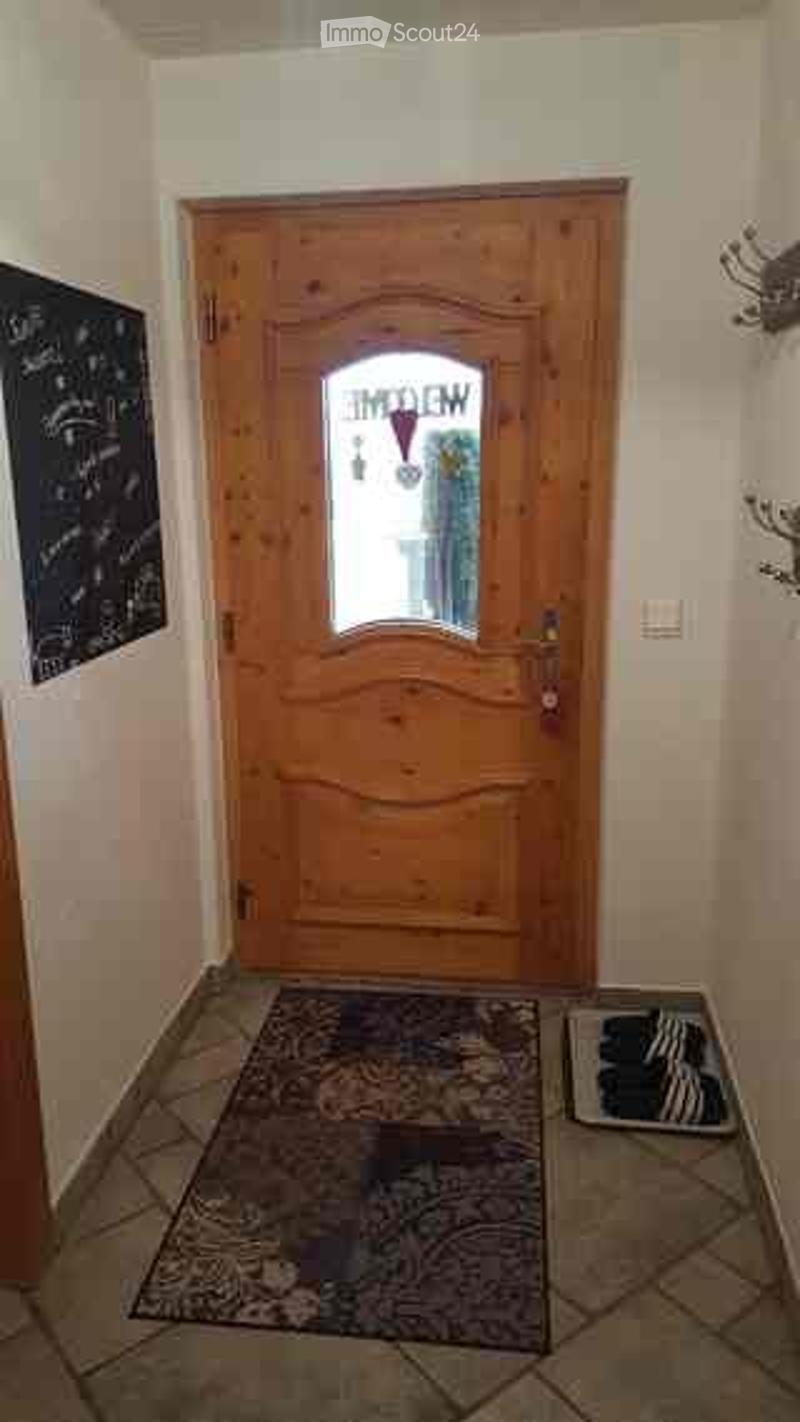 A narrow hallway with a wooden front door featuring a glass panel, a small rug, and a decorative wall piece on the left side.